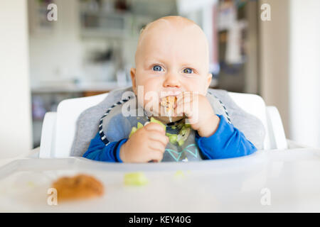 Baby Boy eating bread et concombre avec méthode, BLW led bébé sevrage. Heureux végétariens kid au dîner. Tout-petit manger lui-même, auto-alimentent. Banque D'Images