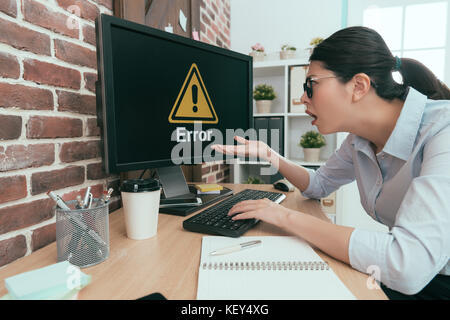 Tristesse suit femme assise sur un bureau de travail à l'aide pour taper sur le clavier de l'ordinateur mais le rapport d'erreur indiquant que son sentiment confus. Banque D'Images