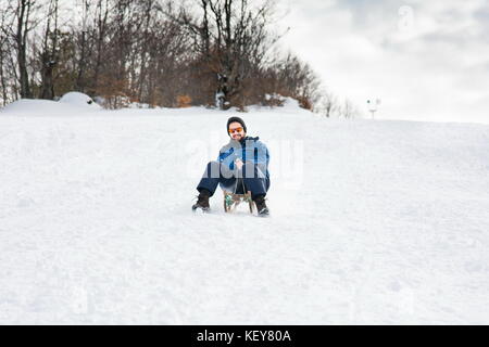 Homme barbu en traîneau sur la neige en bas de la colline Banque D'Images