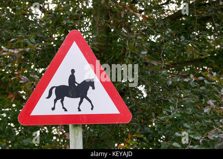 Chevaux et cavaliers en route panneau d'avertissement sur le côté gauche de l'image. cheval noir sur fond blanc en triangle rouge fond vert. Banque D'Images