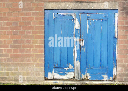 Vieille porte en bois bleu délavé avec peinture feuilletée dans mur de brique rouge avec cadenas et porte-cadenas Banque D'Images