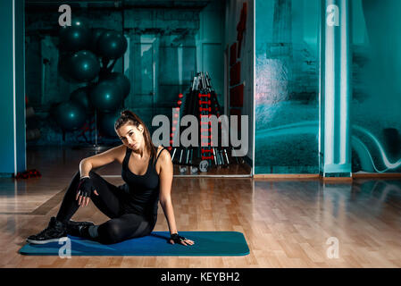 Young attractive brunette femme assise sur le tapis bleu en sport. tonique de l'image. Banque D'Images