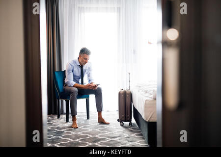 Mature businessman avec un smartphone dans une chambre d'hôtel. bel homme de sms. Banque D'Images