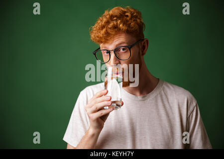 Curly readhead beau barbu à lunettes, eau potable, looking at camera, sur fond vert. Banque D'Images