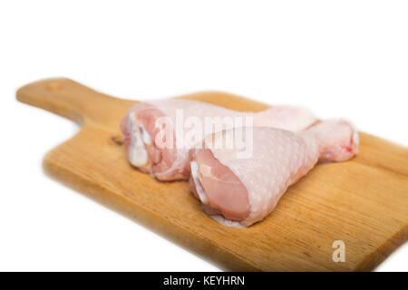 Deux pilons de poulet crus sur une planche à découper sur un fond blanc Banque D'Images