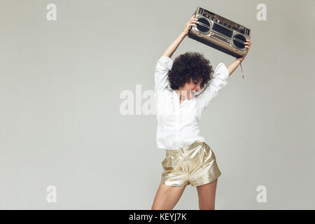 Les jeunes cris émotionnels retro femme vêtue de shirt debout et posant isolé. À côté de radiocassette holding. Banque D'Images
