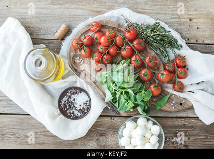 Basilic, tomates cerise, mozzarella, huile d'olive, sel, épices rustique sur planche à découper Banque D'Images