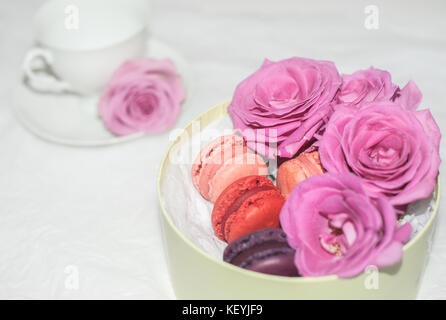 Un thé blanc à la rose d'un côté, macarons et roses roses dans une boîte-cadeau Banque D'Images