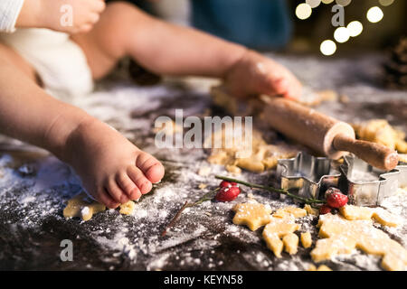 Jeune famille making gingerbread cookies à la maison. méconnaissable petit bébé assis sur la table. l'occasion de Noël. Banque D'Images