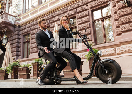 Vue latérale sur toute la longueur de l'image déplut business man sitting on barbu moto moderne en plein air avec femme élégante qui à miroir à Banque D'Images