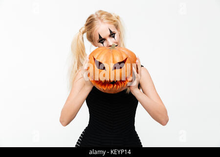 Portrait d'une femme blonde espiègle dans halloween composent se cacher derrière une citrouille - isolated over white background Banque D'Images