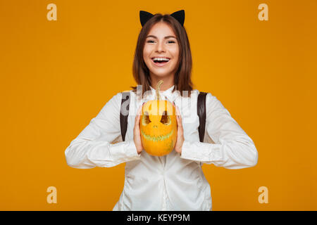 Portrait of a smiling teenage lycéenne en uniforme avec sac à dos tenue halloween citrouille et à la caméra au plus isolé sur fond orange Banque D'Images