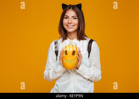 Portrait of a Teenage lycéenne en uniforme avec sac à dos tenue halloween citrouille et à la caméra au plus isolé sur fond orange Banque D'Images