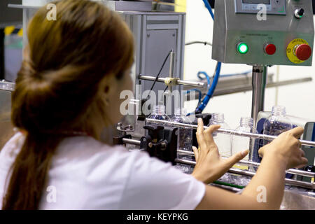 Unidentify femme asiatique de placer la nouvelle bouteille en plastique vide dans la chaîne de production de l'eau machine dans l'usine d'eau potable. Mise au point sélective. Banque D'Images