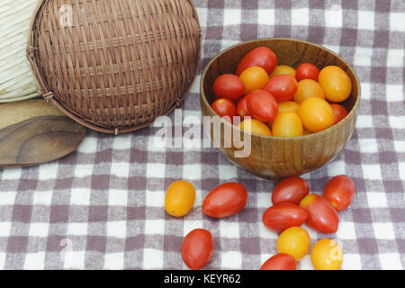 Les petites tomates cerises rouges débordent d'un panier en osier sur une vieille table en bois dans un style rustique, selective focus Banque D'Images