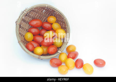 Les petites tomates cerises rouges et jaunes débordent d'un panier en osier isolées sur fond blanc Banque D'Images