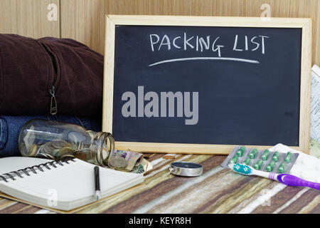 Travel concept. liste de colisage sur tableau noir avec des vêtements,,médecine,compas,brosse à dents,crayon carnet vide et de l'argent tomber du bocal en verre. Banque D'Images