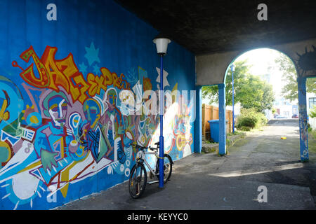 Bike leaning against blue lampadaire et arcade avec graffiti sur mur lumineux dans le vieux quartier du port de Reykjavik, capitale de l'islande Banque D'Images