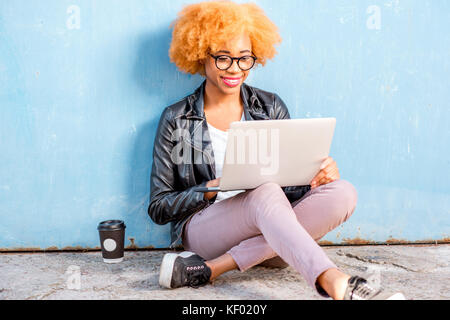 Femme africaine avec l'ordinateur portable sur le fond bleu Banque D'Images