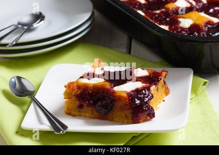 Morceau de gâteau avec fromage cottage et confiture de fruits sur une petite assiette blanche. Plus de plaques et plaque de cuisson noire avec le gâteau en arrière-plan Banque D'Images