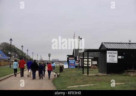 Les gens qui marchent le long du front de mer d'Aldeburgh devant les cabanes des pêcheurs. Suffolk, Royaume-Uni. Banque D'Images