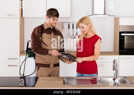 Jeune femme souriante de facture signature travailleur exterminateur après travaux antiparasitaires en cuisine maison Banque D'Images