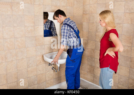 Handyman installation lavabo avec jeune femme se tenir dans la salle de bains Banque D'Images