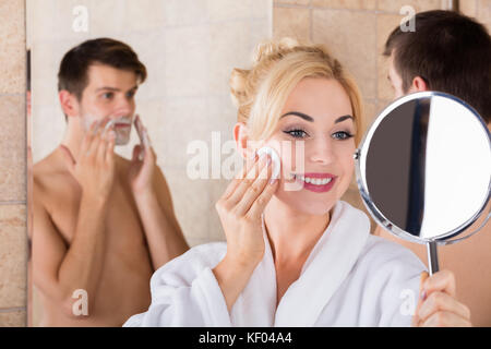 Portrait d'un homme et son épouse de rasage nettoyer son visage en miroir d'une salle de bains privative Banque D'Images