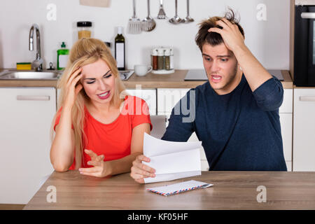 Jeune couple inquiet lisant la lettre et le projet de loi dans la cuisine à la maison. Concept de mauvaises nouvelles Banque D'Images