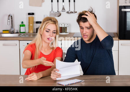 Jeune couple inquiet pour lire une lettre envoyée avec une mauvaise loi dans la cuisine à la maison Banque D'Images