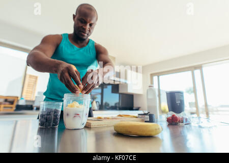 L'homme préparer milk shake en cuisine. L'homme athlétique ajout de fruits pot de lait. Banque D'Images