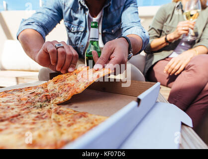 Close up de pizza sur la table avec de jeunes gens assis autour et en ramassant une partie. La fête d'amis sur le toit et de manger des pizzas. Banque D'Images