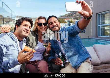 Jeunes amis en tenant sur un téléphone intelligent selfies lors d'une partie. Les jeunes de manger des pizzas et boire des bières sur le toit partie prenant. selfies Banque D'Images