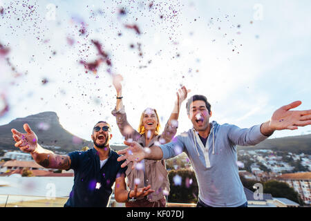 Groupe de professionnels jeunes jetant des confettis tout en appréciant rooftop party. Les amis s'amusant à Terrace, à soir. Banque D'Images