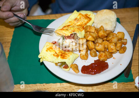 Obscure personne tenant en main la fourchette sur une assiette blanche et napperon rempli d'aliments gras assortis sur table Banque D'Images