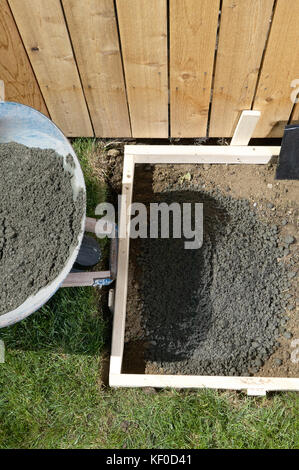 Un jardin, bricolage accueil Projet de bâtiment en béton close up avec le ciment mouillé, clôture en bois, une brouette et forme de travail. Banque D'Images