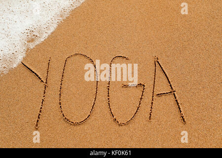 Le mot yoga écrit dans le sable d'une plage, avec vue sur la mer dans un coin de mousse Banque D'Images