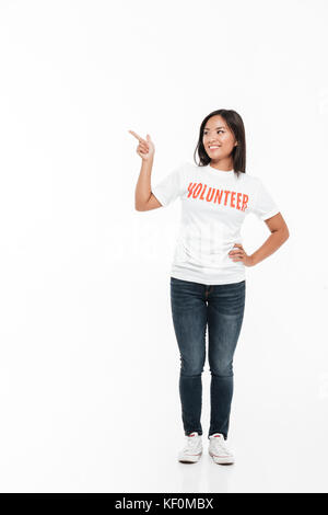 Portrait d'une jolie femme asiatique joyeuse en t-shirt et en pointant du doigt à copie espace isolated over white backgroun Banque D'Images