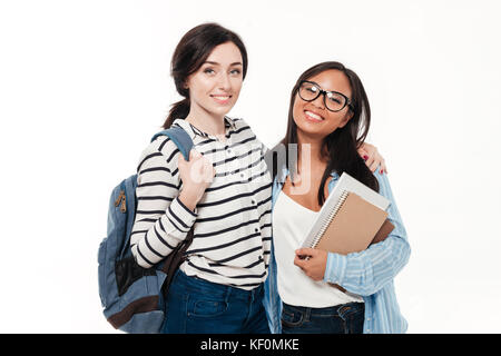 Couple de deux étudiantes multiethnique souriant avec sac à dos et books hugging and looking at camera isolated over white background Banque D'Images