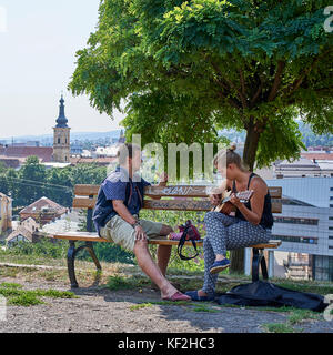 Couple assis sur un banc en bois avec vue sur la ville de Cluj, la femme en jouant de la guitare et chant Banque D'Images