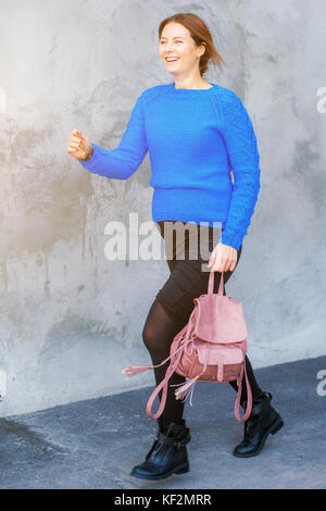 Une belle femme enceinte dans une auto-tricoté bleu portant un chandail, une jupe étroite noire et un sac à dos rose beige gris le long d'une peint inégalement wal Banque D'Images