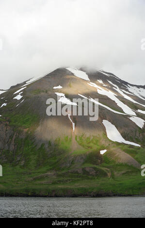 Taches de neige et herbe verte sur la montagne avec ciel nuageux à Siglufjordur, Nord de l'Islande, Scandinavie Banque D'Images