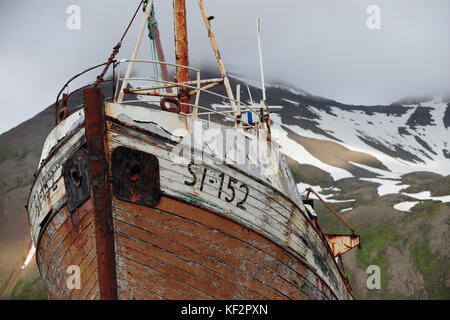 Bateau rouillé abandonné altérées avec l'écaillage de la peinture en ship yard de siglufjordur ville à distance avec des montagnes enneigées en arrière-plan, le nord de l'islande Banque D'Images