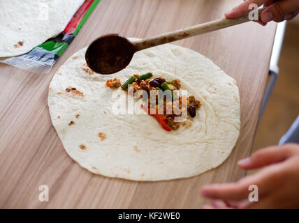 La préparation, maison burrito main femme remplissant tortilla avec mélange de viande et de légumes dans la cuisine. Banque D'Images