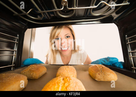 Jeune femme souriante insérant des biscuits plateau dans le four à la cuisine Banque D'Images