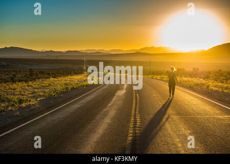 Femme marchant sur une longue route sinueuse au coucher du soleil dans l'est du Nevada, USA Banque D'Images