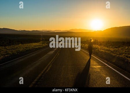 Femme marchant sur une longue route sinueuse au coucher du soleil dans l'est du Nevada, USA Banque D'Images