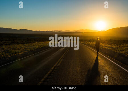 Femme marchant sur une longue route sinueuse au coucher du soleil dans l'est du Nevada, USA Banque D'Images