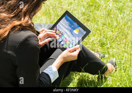 Close-up of businesswoman sitting on grass using digital tablet with applications multicolores sur elle Banque D'Images