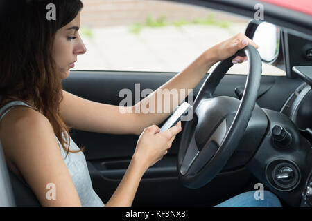 Side view of young woman using mobile phone while driving car Banque D'Images